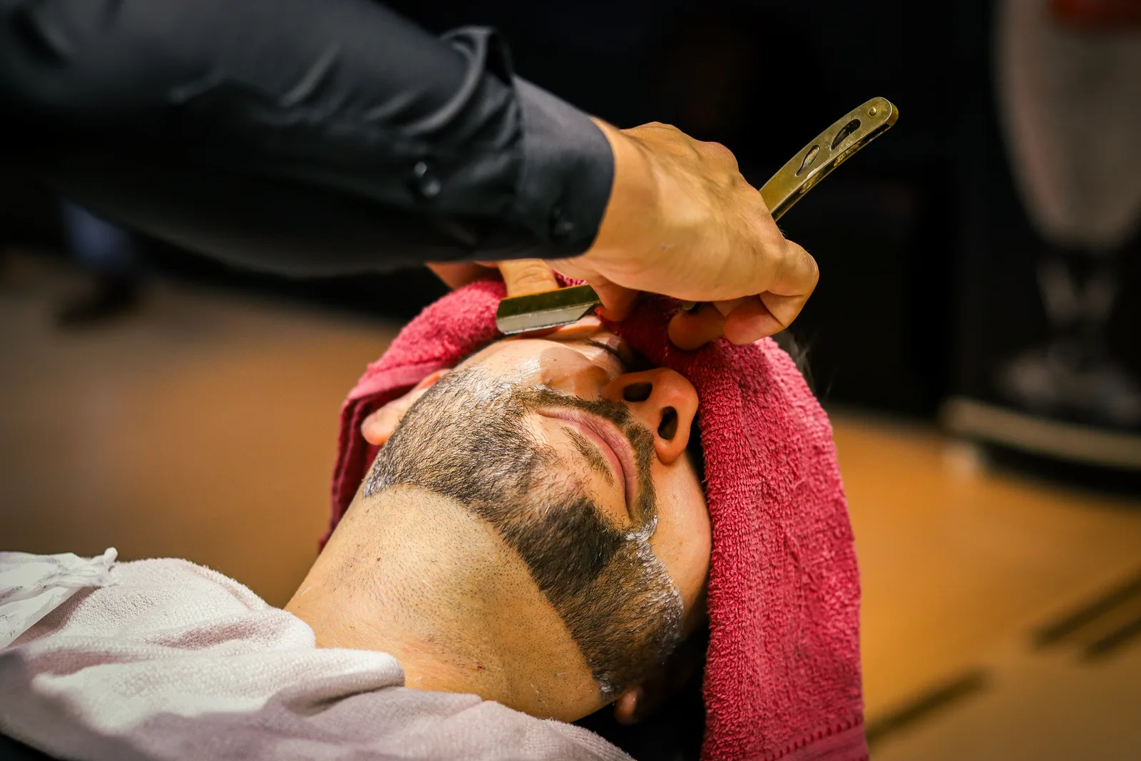 Barbeiro fazendo acabamento de barba em cliente reclinado